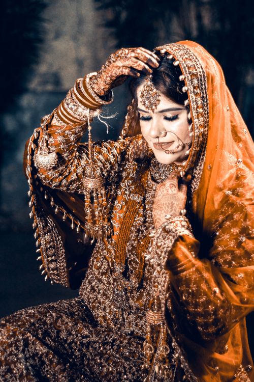 Free A beautiful South Asian bride in a richly adorned orange bridal outfit with intricate henna designs. Stock Photo