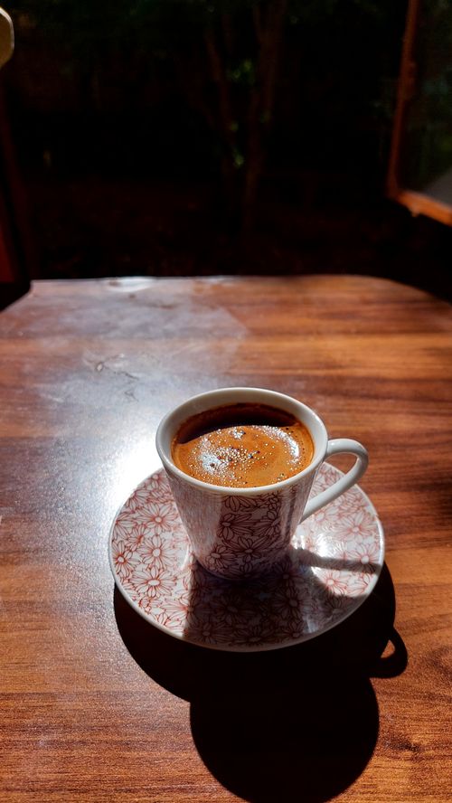 Free A porcelain cup of espresso glistening in sunlight on a wooden table. Stock Photo