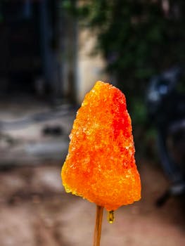 Vibrant orange ice lolly held outdoors, showcasing bold colors and summer vibes.