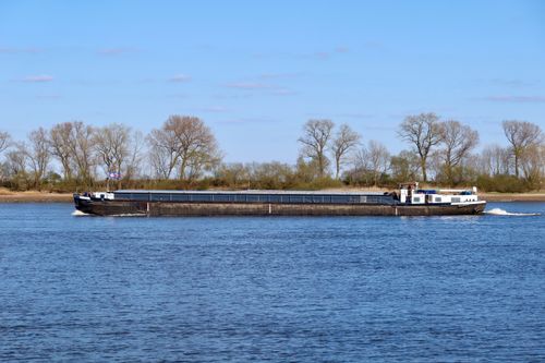 Free A cargo barge sails along a calm river with trees in the background on a clear spring day. Stock Photo