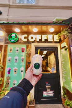 Hand holding iced coffee in front of an Azerbaijani cafe. Vibrant and inviting.