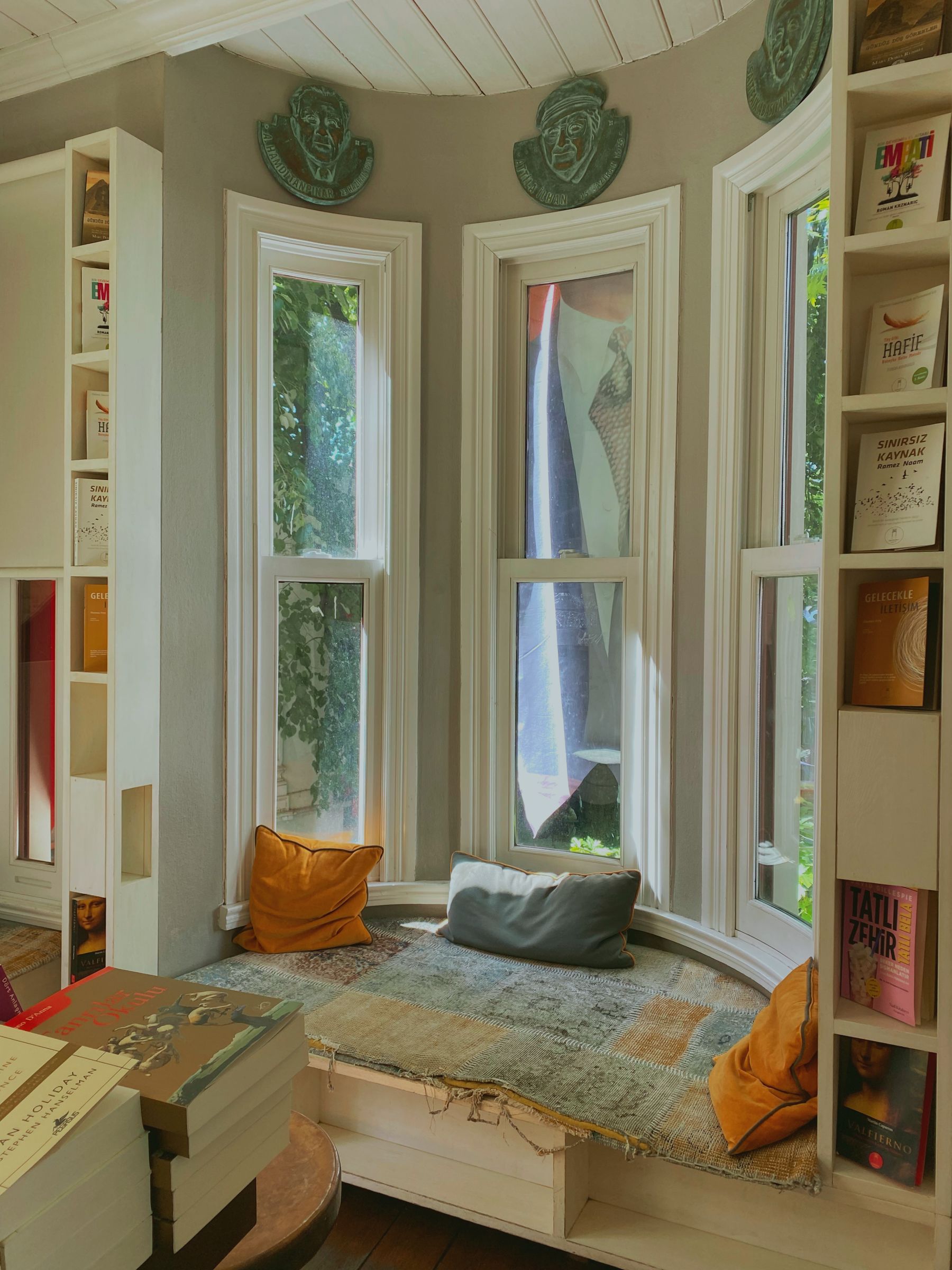 A cushioned bay window seat nestled between bookshelves with tall daylight-filled windows