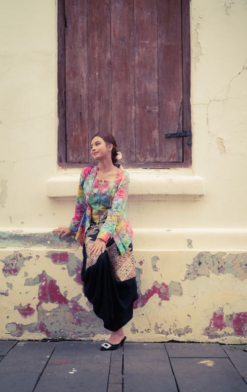 Free A woman in colorful traditional attire leans against a textured wall, evoking cultural and vintage vibes. Stock Photo