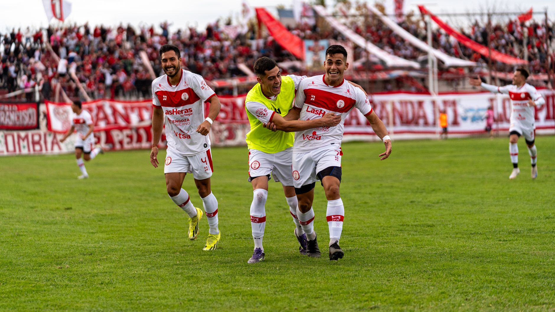 Football players celebrating on the field with an enthusiastic crowd in the background.