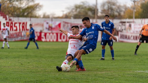 Two players fiercely tackle for the ball in a competitive outdoor soccer match.