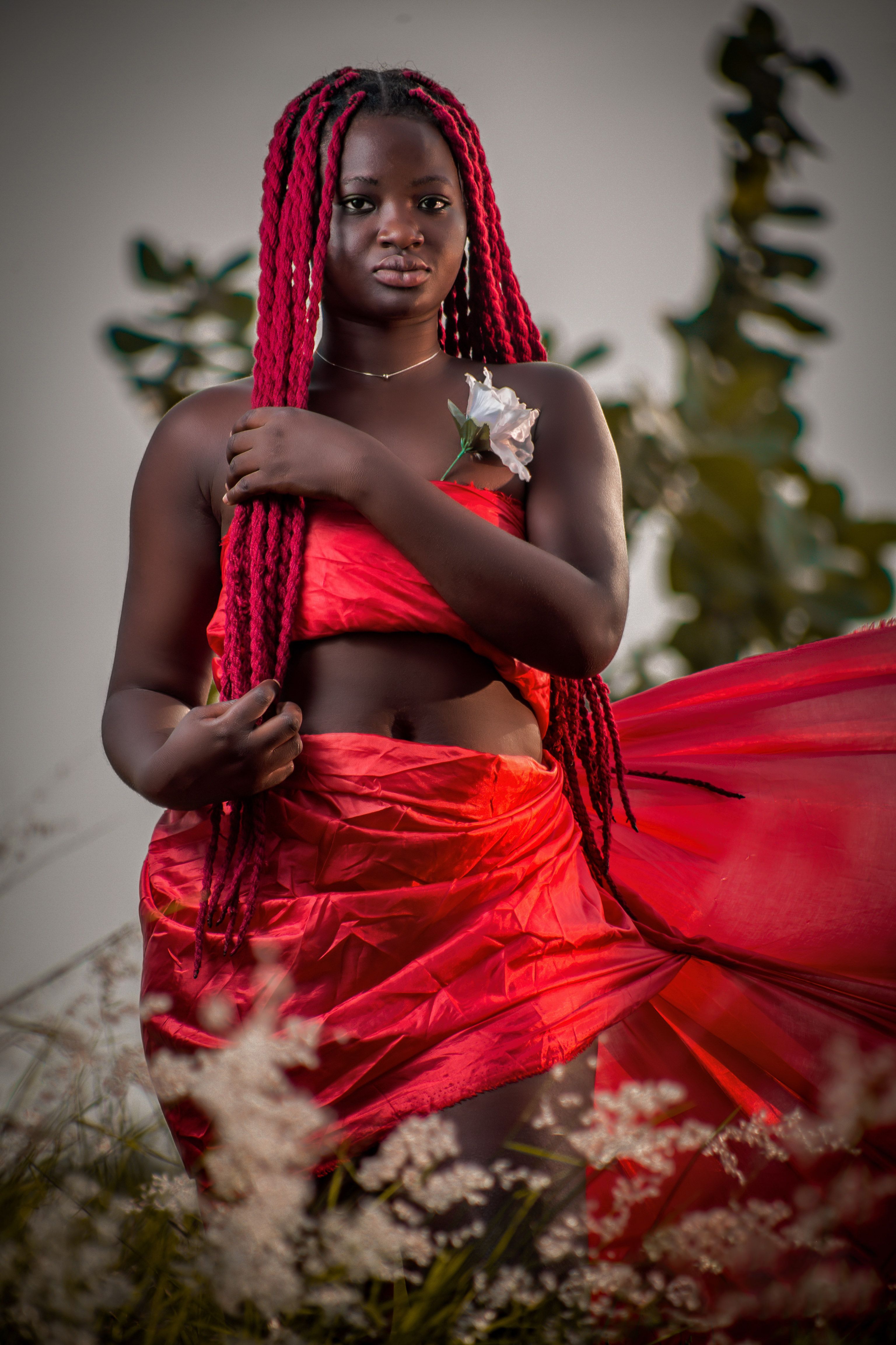 Powerful outdoor portrait of a woman in a flowing red dress surrounded by nature in Ghana.