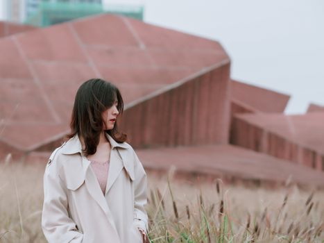 一位时尚女性站在现代建筑旁，若有所思地望向一边