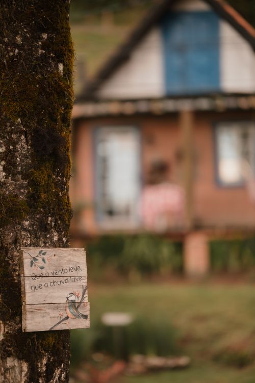 Free Charming rustic scene with a weathered sign on a tree and blurred cottage in the background. Stock Photo