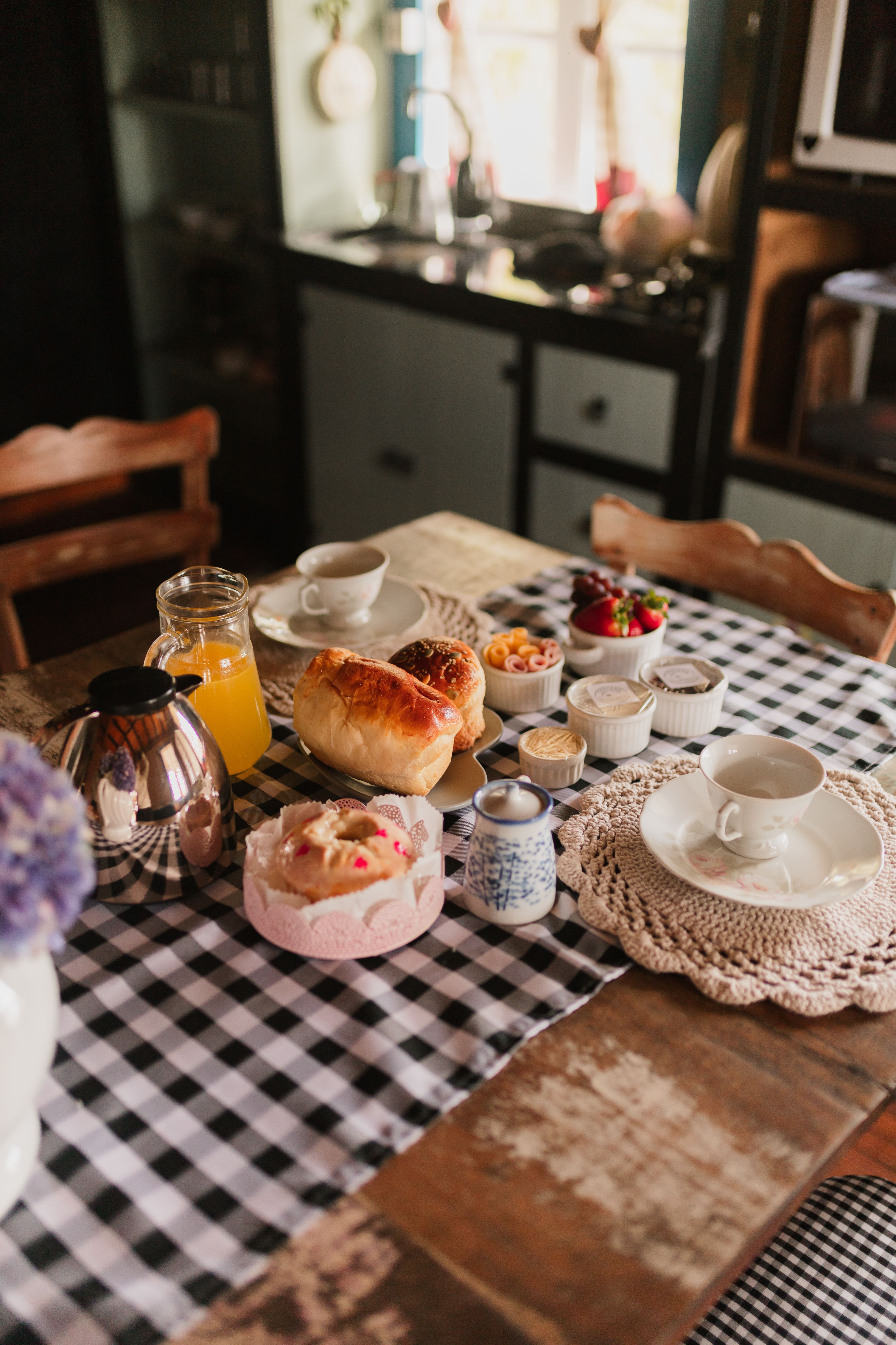 A delightful country-style breakfast with pastries, tea, and juice on a checkered tablecloth in a cozy kitchen.