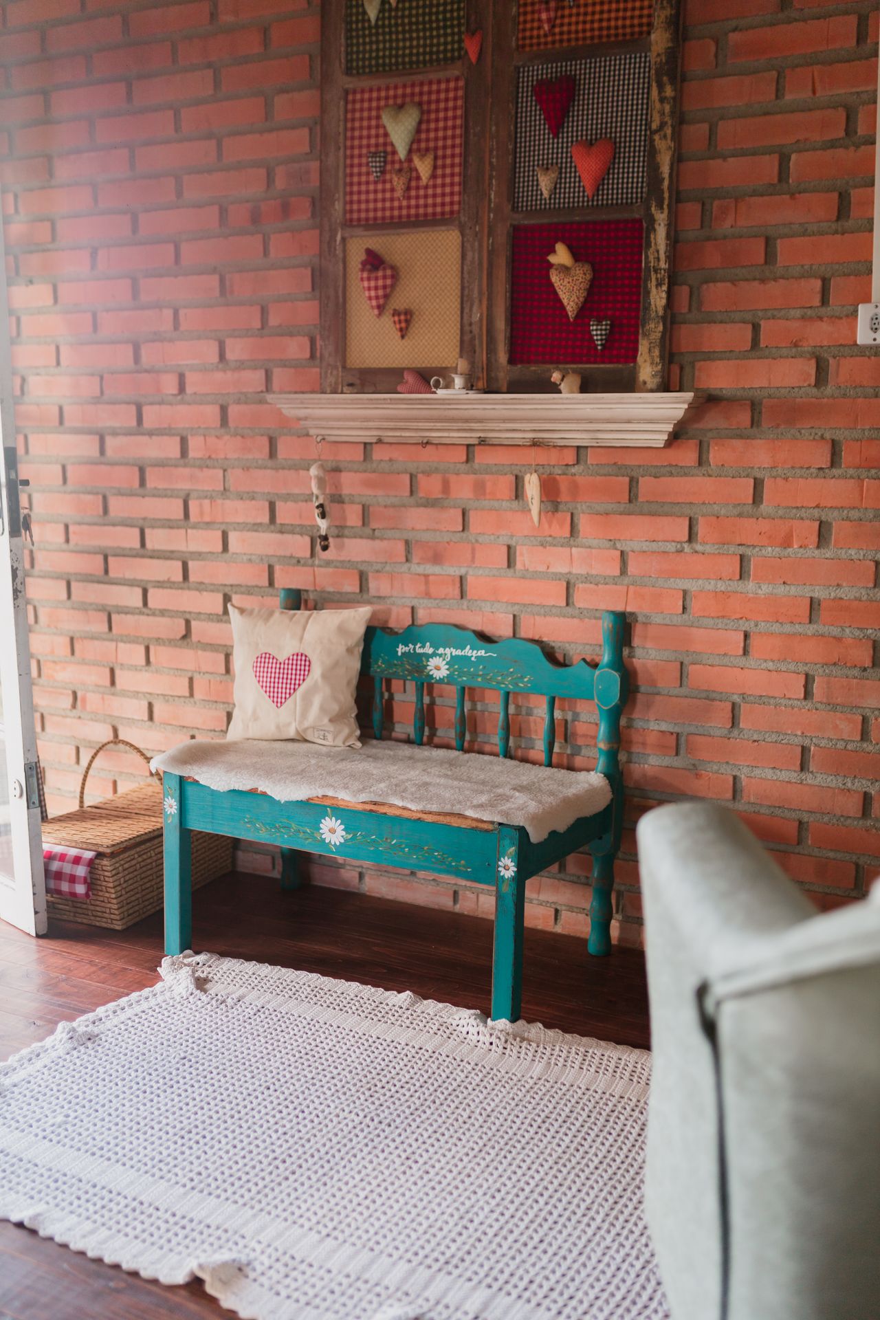 Painted teal wooden bench with heart details against a warm brick wall, with a crochet rug on the floor
