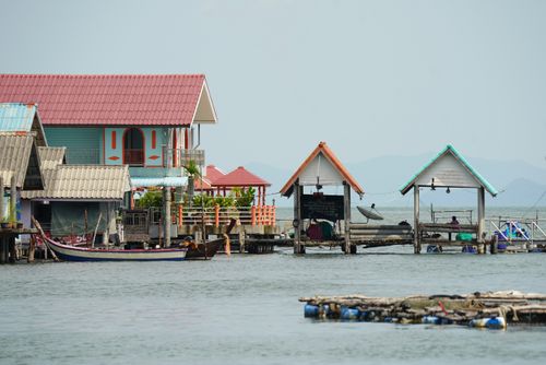 Free Scenic view of vibrant houses on stilts over calm coastal waters with distant mountains. Stock Photo