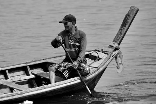 Free A fisherman rows his boat across a lake, showcasing traditional fishing methods in a serene setting. Stock Photo