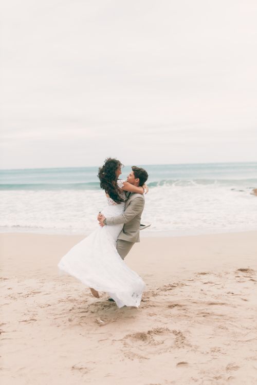 Free A couple shares a joyful embrace on a scenic sandy beach during their wedding. Stock Photo
