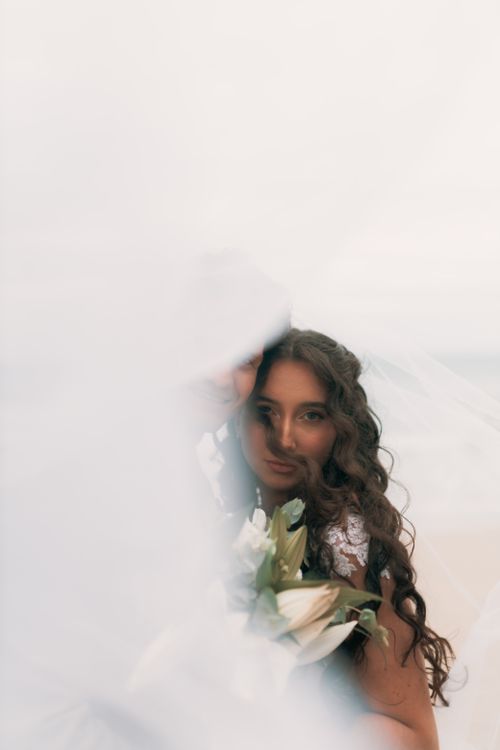 Free Elegant bride with bouquet and veil, dreamy beach setting. Stock Photo