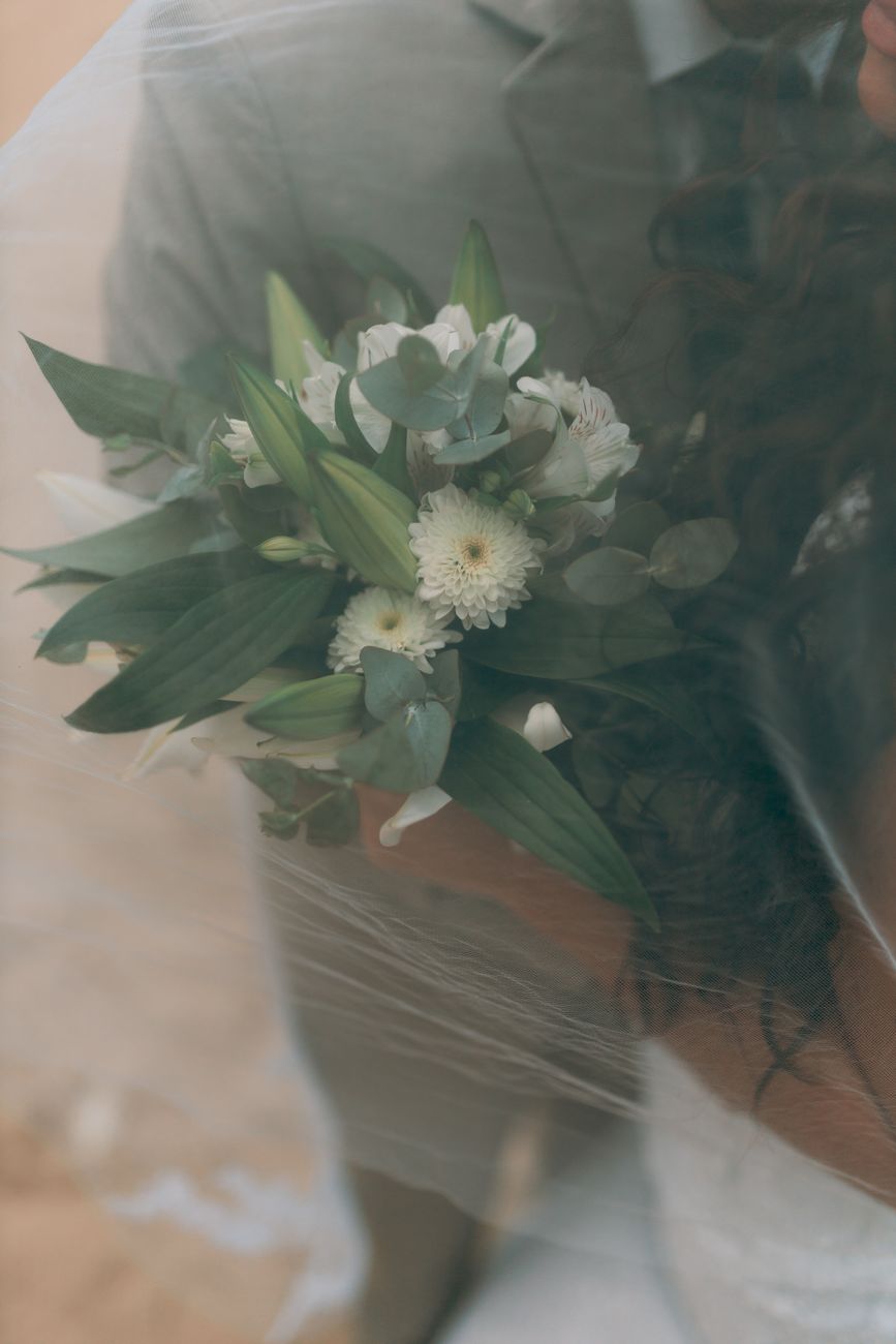 Close-up of a bride's bouquet featuring white and green flowers under a veil, creating a romantic atmosphere.