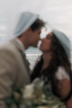 Artistic beach wedding photo of a couple kissing with a soft focus effect.