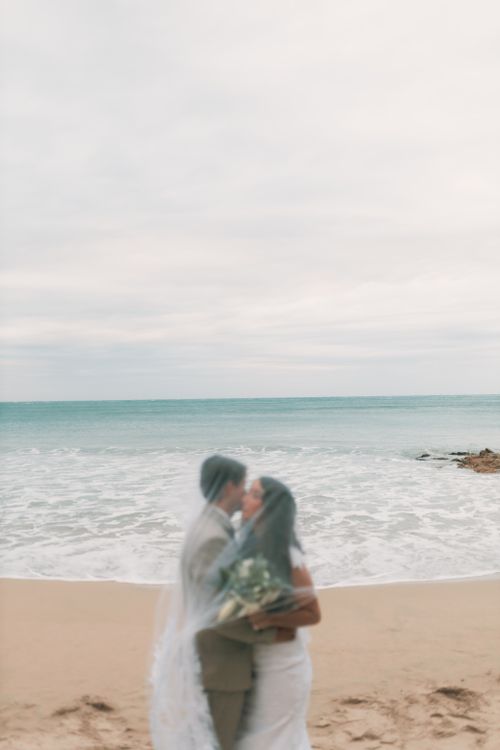 Free Blurred couple kissing by the ocean on a sandy beach, romantic wedding scene. Stock Photo