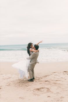 A joyful bride and groom share a romantic embrace on a sandy beach.