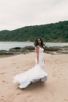 Elegant bride in white dress on sandy beach with ocean view. Captured with natural ambiance.