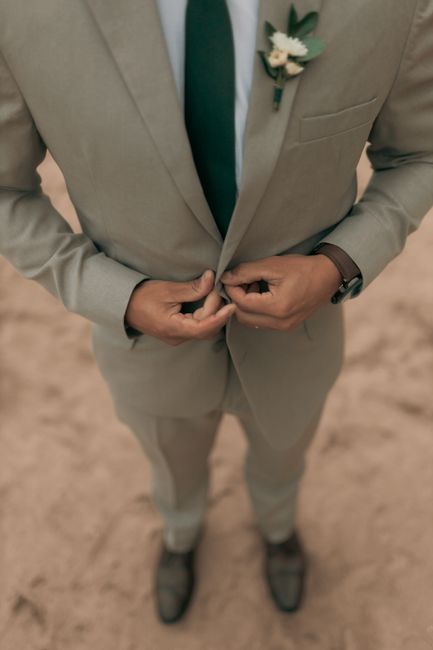 Stylish groom adjusting his suit button on a sandy beach. Perfect for wedding themes.