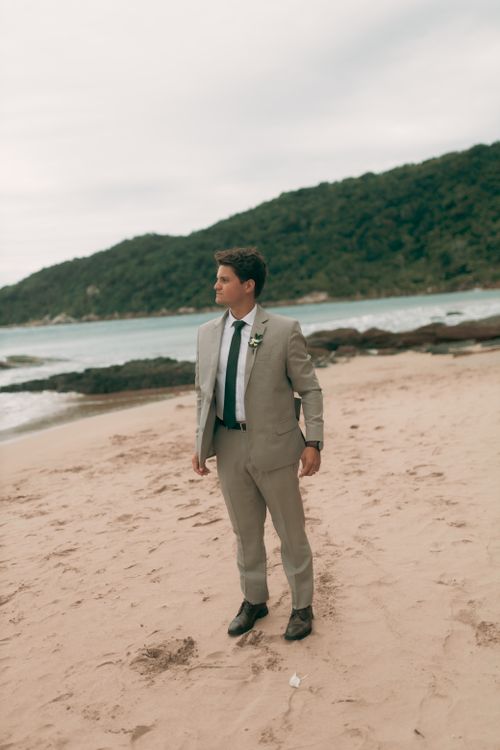 Free A man in a light suit stands on a beach with scenic hills in the background. Stock Photo