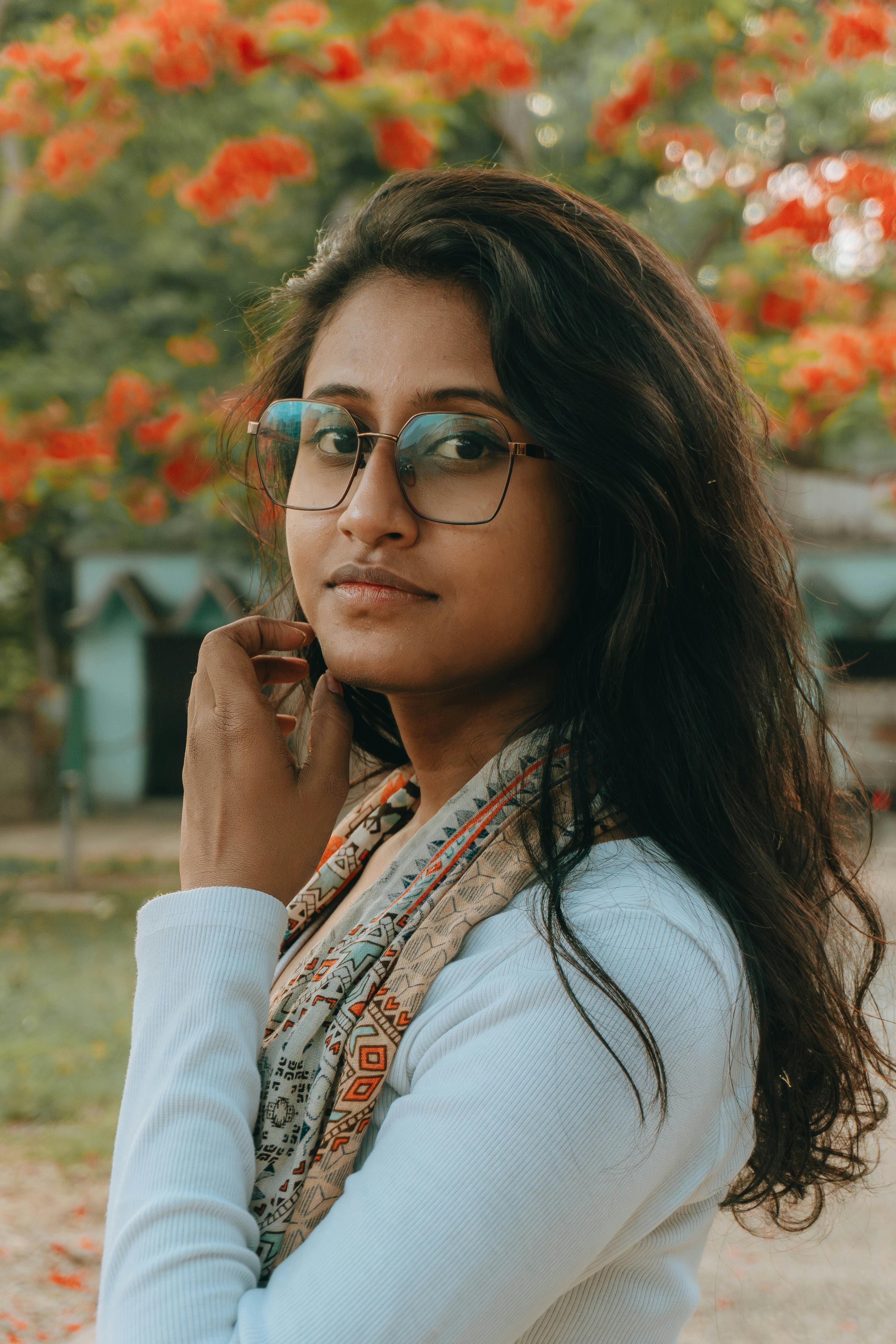 Captivating portrait of a young woman with glasses in a colorful garden, exuding natural elegance.