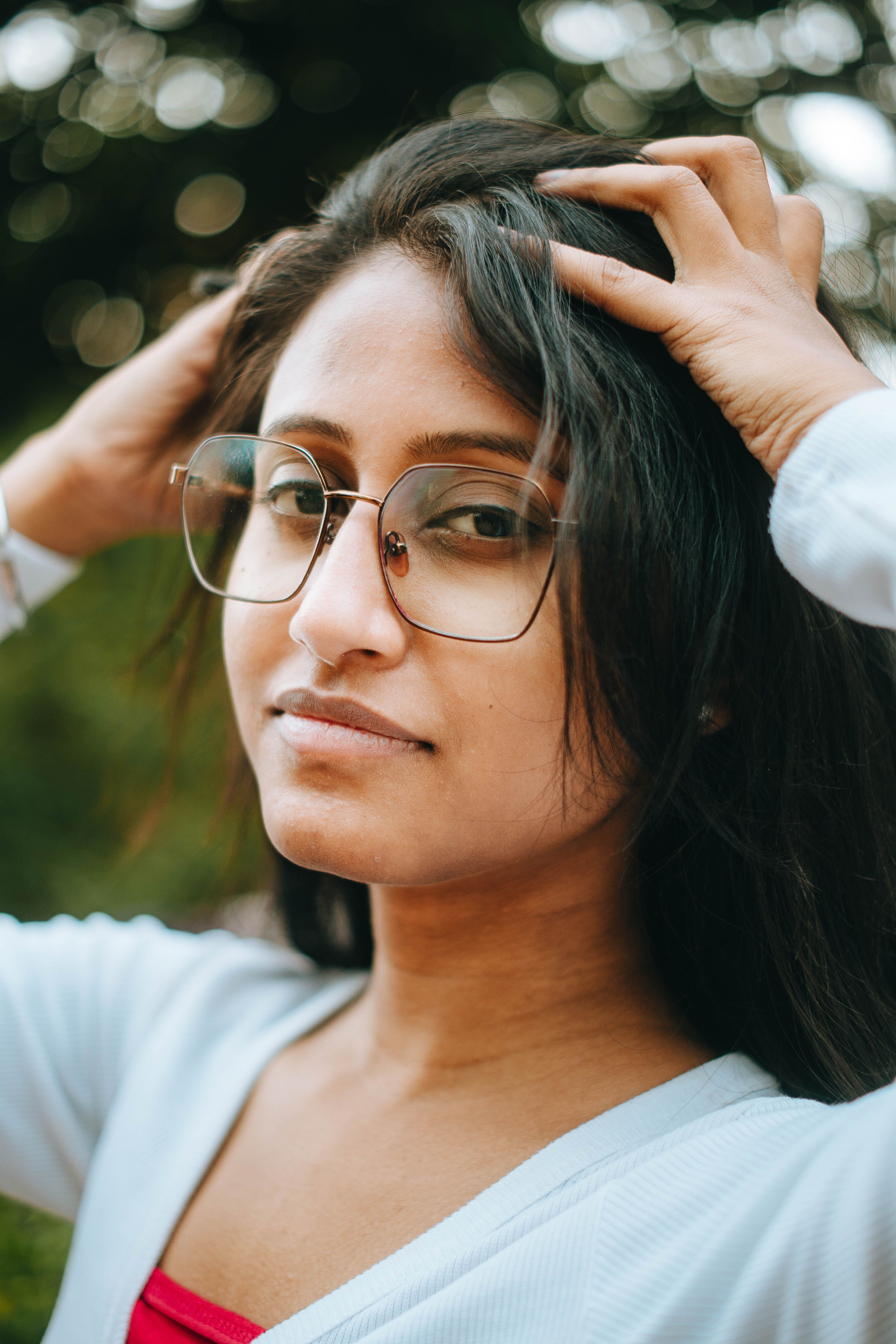 Close-up of a young woman with glasses adjusting her hair outdoors, showcasing a confident and natural look.