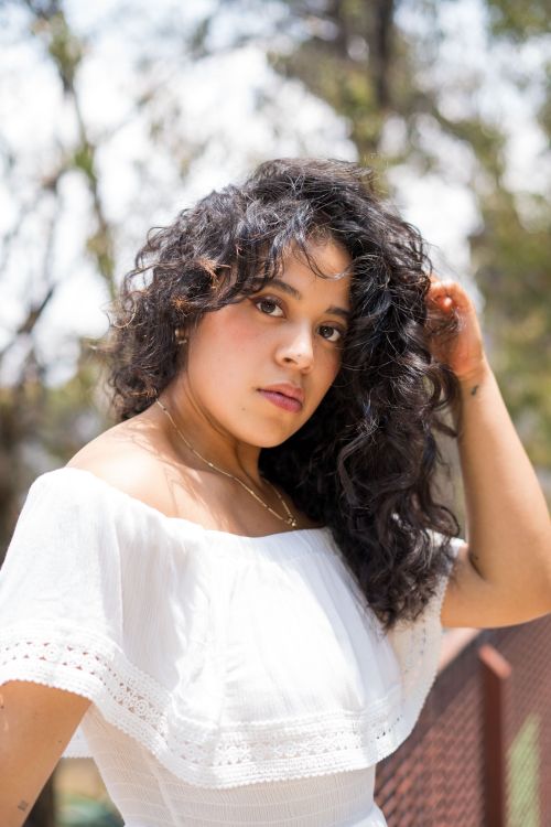 Free Captivating outdoor portrait of a woman with curly hair and white dress in sunlight. Stock Photo
