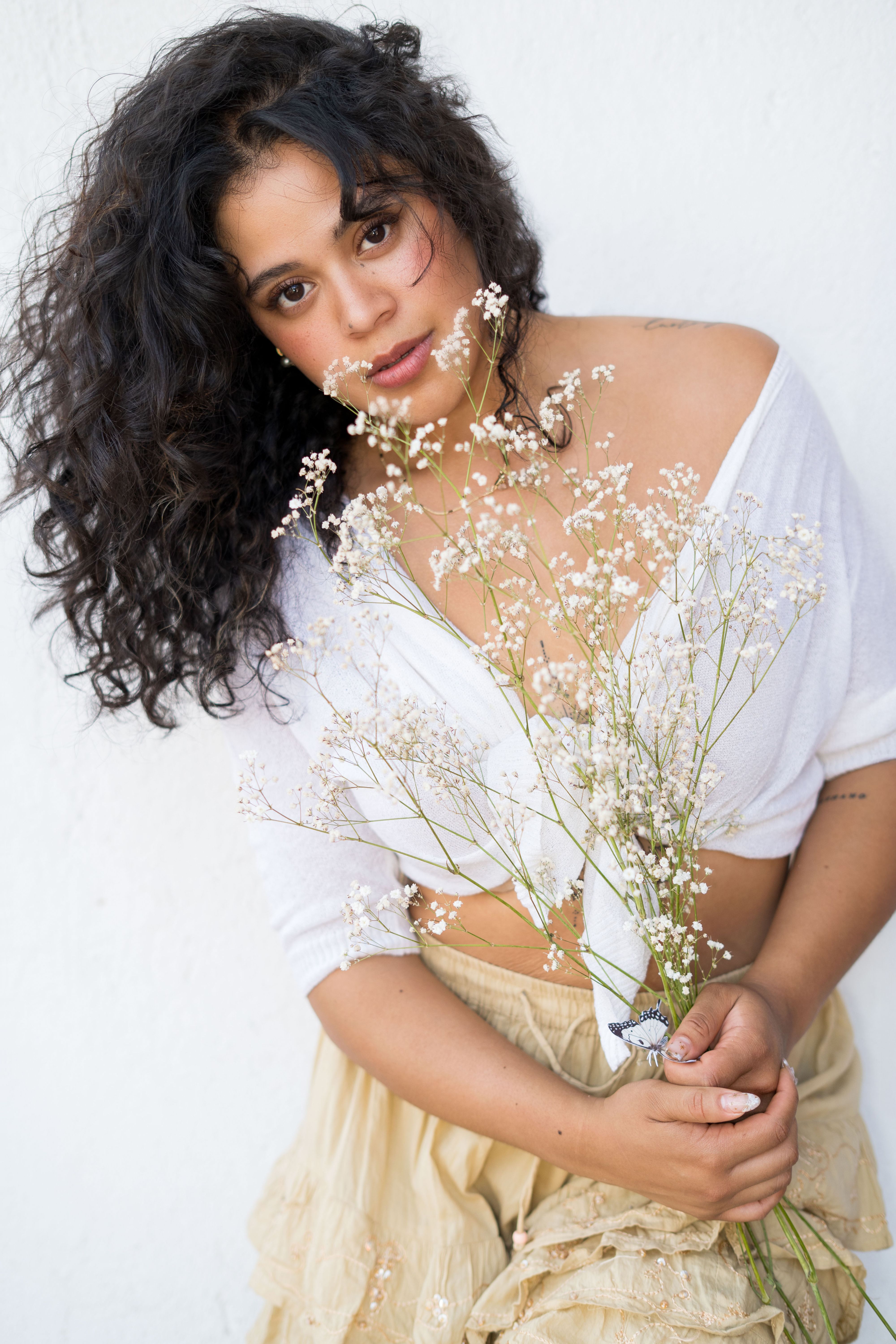 Young woman with curly hair holding delicate baby's breath flowers, wearing light clothing.
