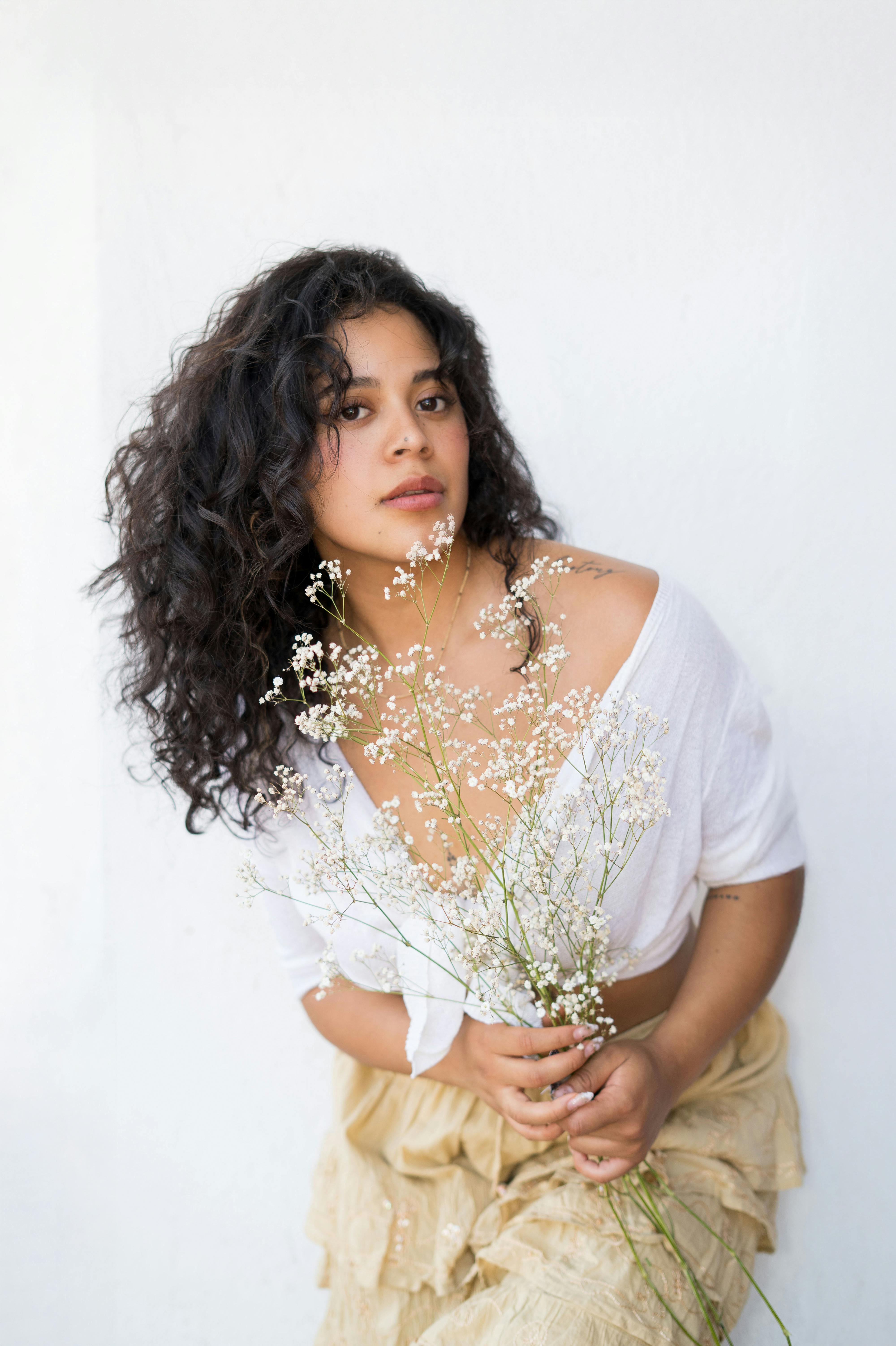 Elegant portrait of a woman with curly hair holding delicate wildflowers against a light background.