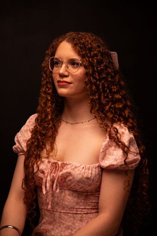 Free Portrait of a young woman with curly hair wearing a pink floral dress with glasses. Stock Photo