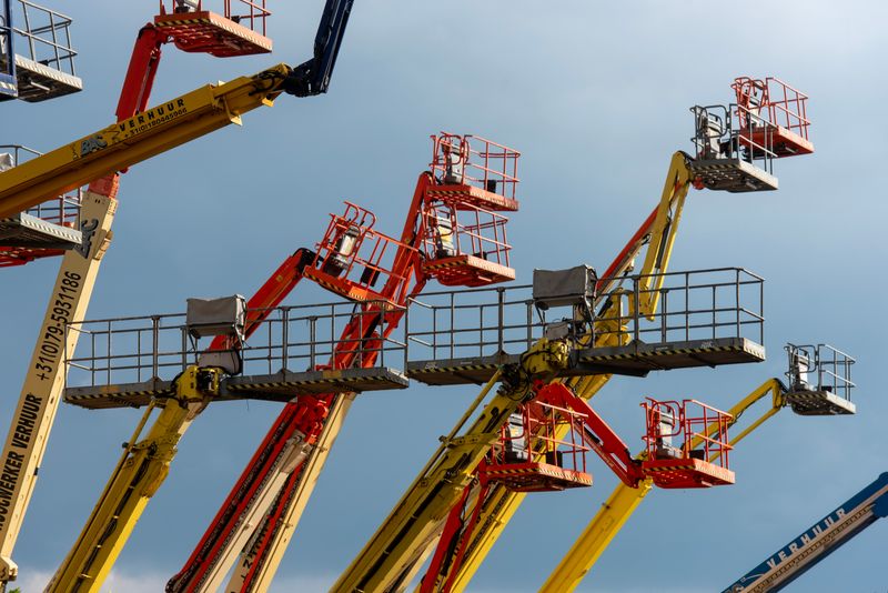 Vibrant boom lifts reaching skyward, showcasing industrial machinery against a clear blue backdrop