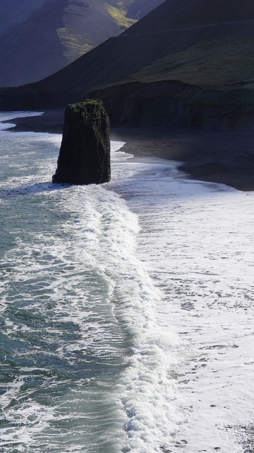 Free Scenic view of Iceland's coastline featuring a prominent sea stack and waves. Stock Photo