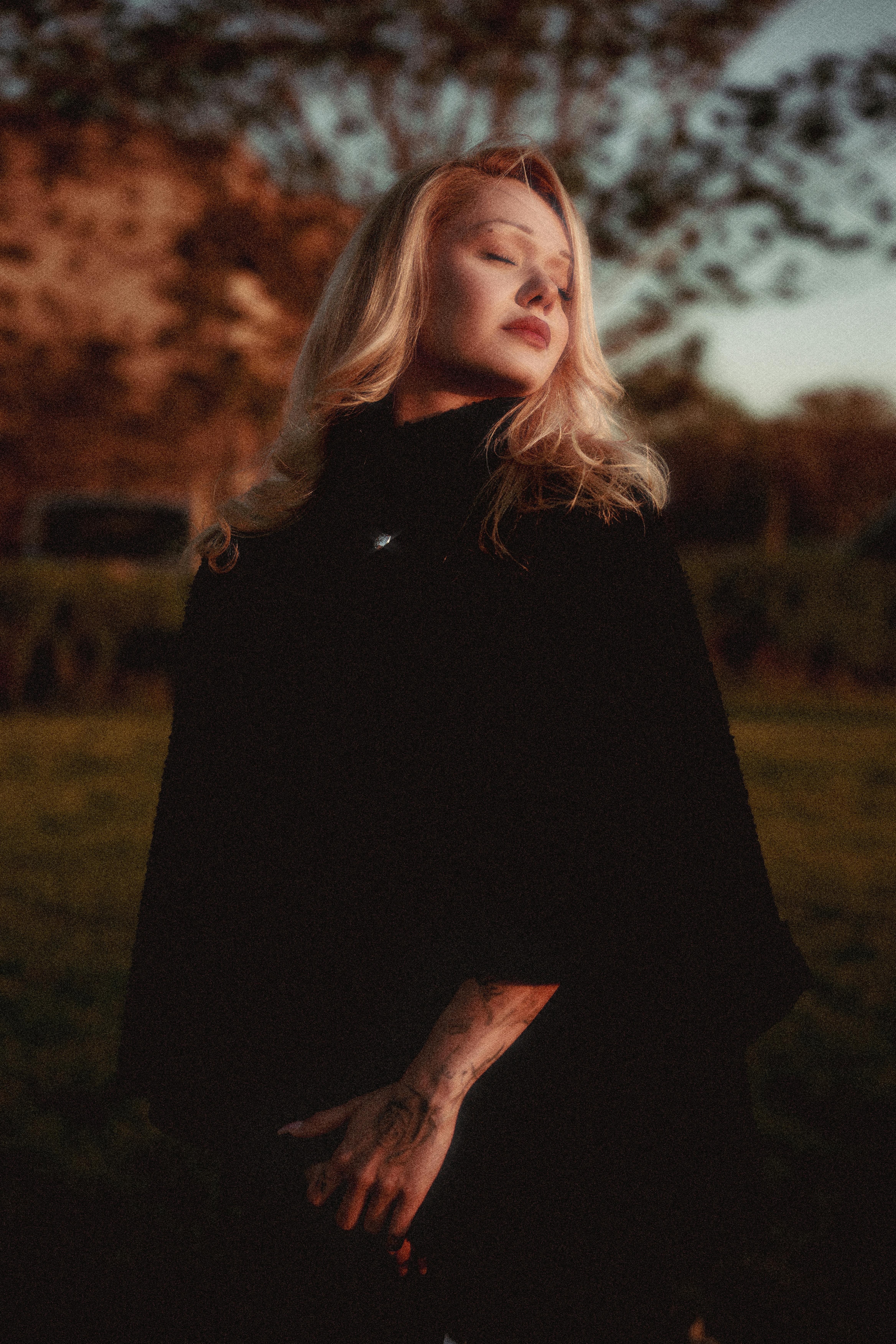 A serene woman enjoying the warm glow of sunset in a tranquil outdoor setting.