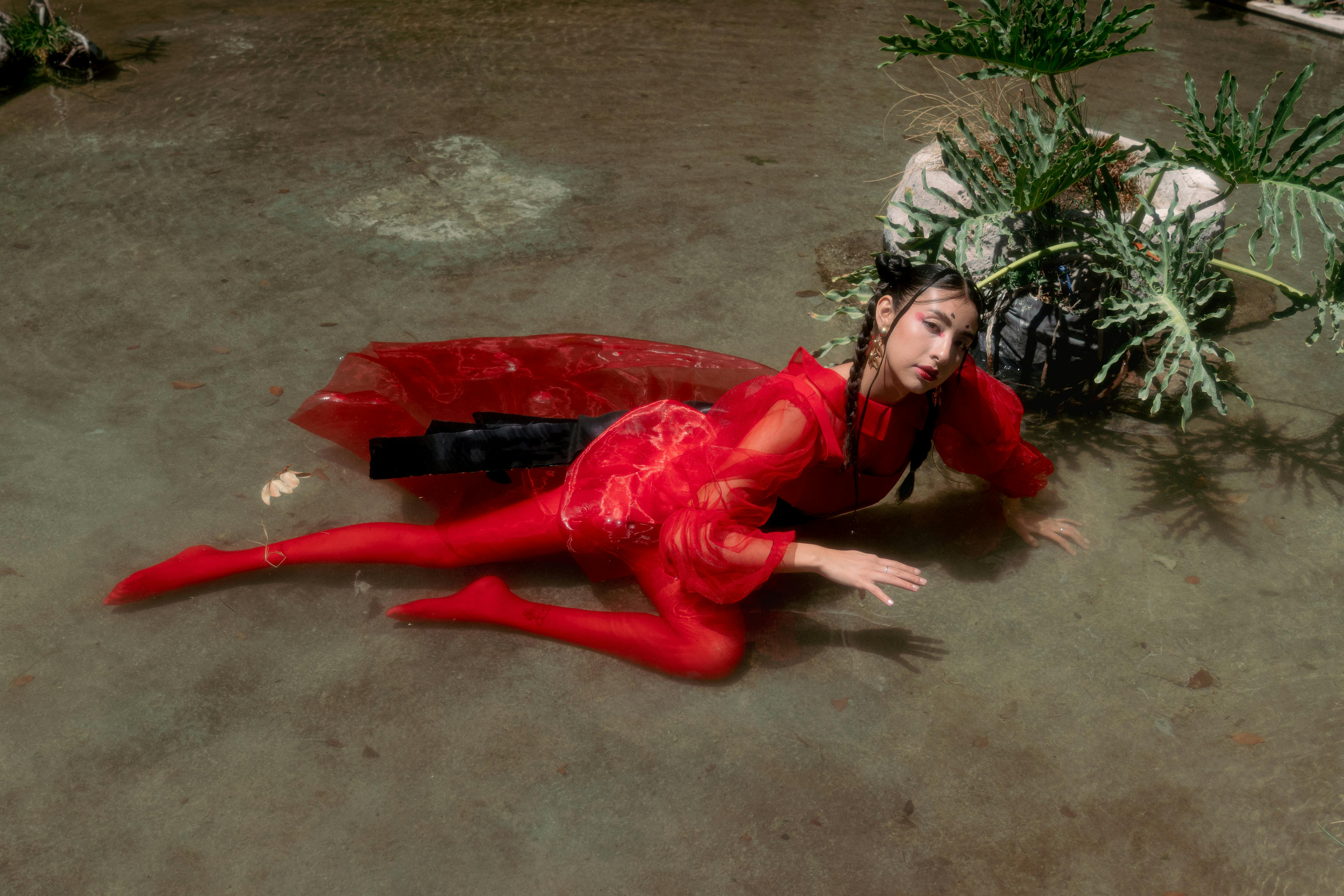 Free Striking fashion editorial featuring a model in red attire posing in shallow water. Stock Photo