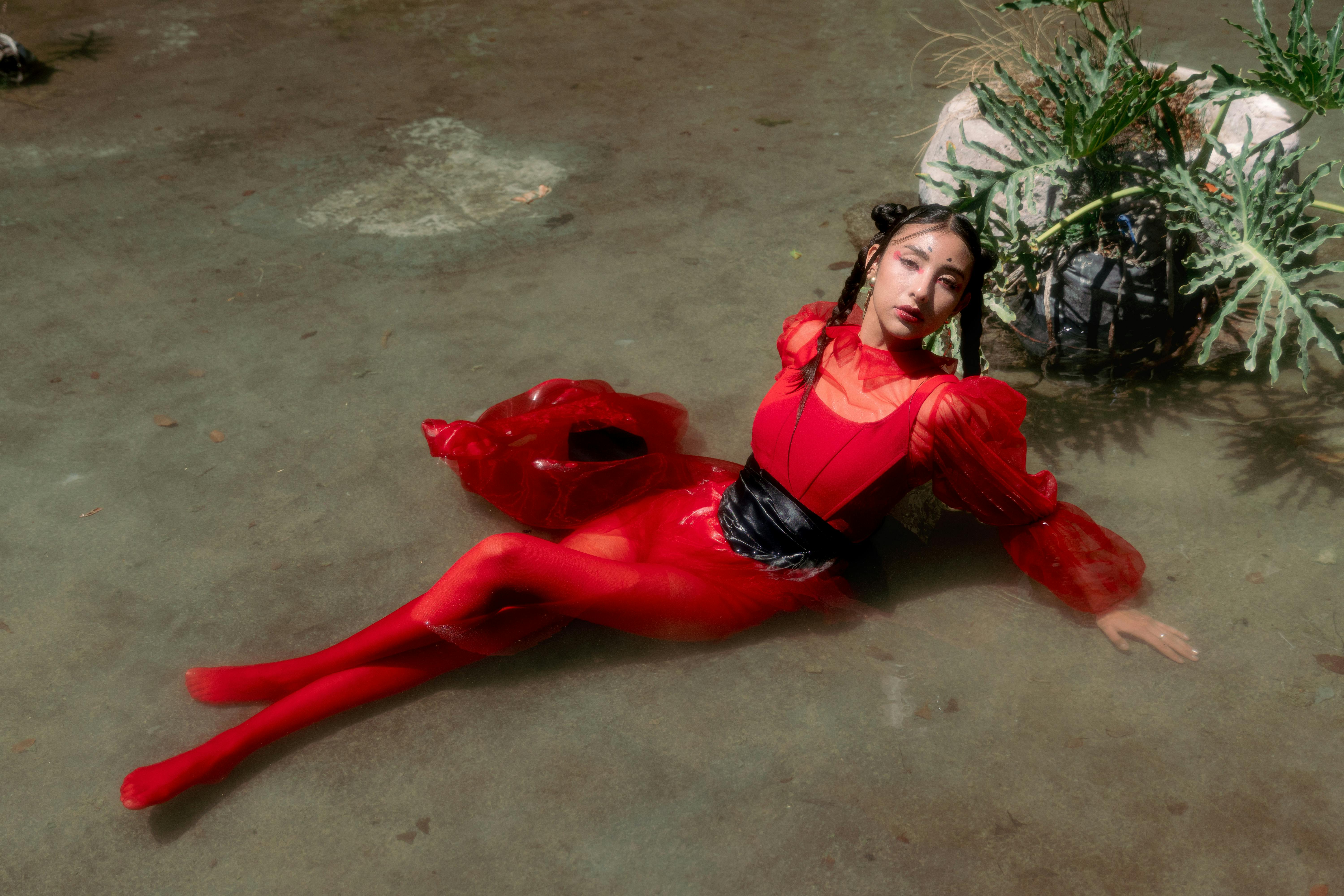 Striking editorial shot of a model in a vibrant red dress posing in water.