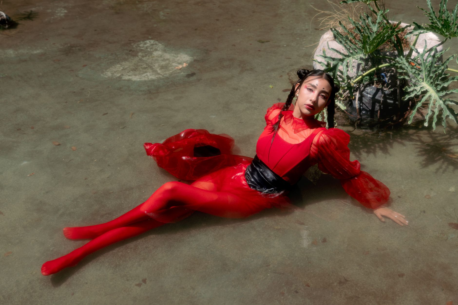 Striking editorial shot of a model in a vibrant red dress posing in water.