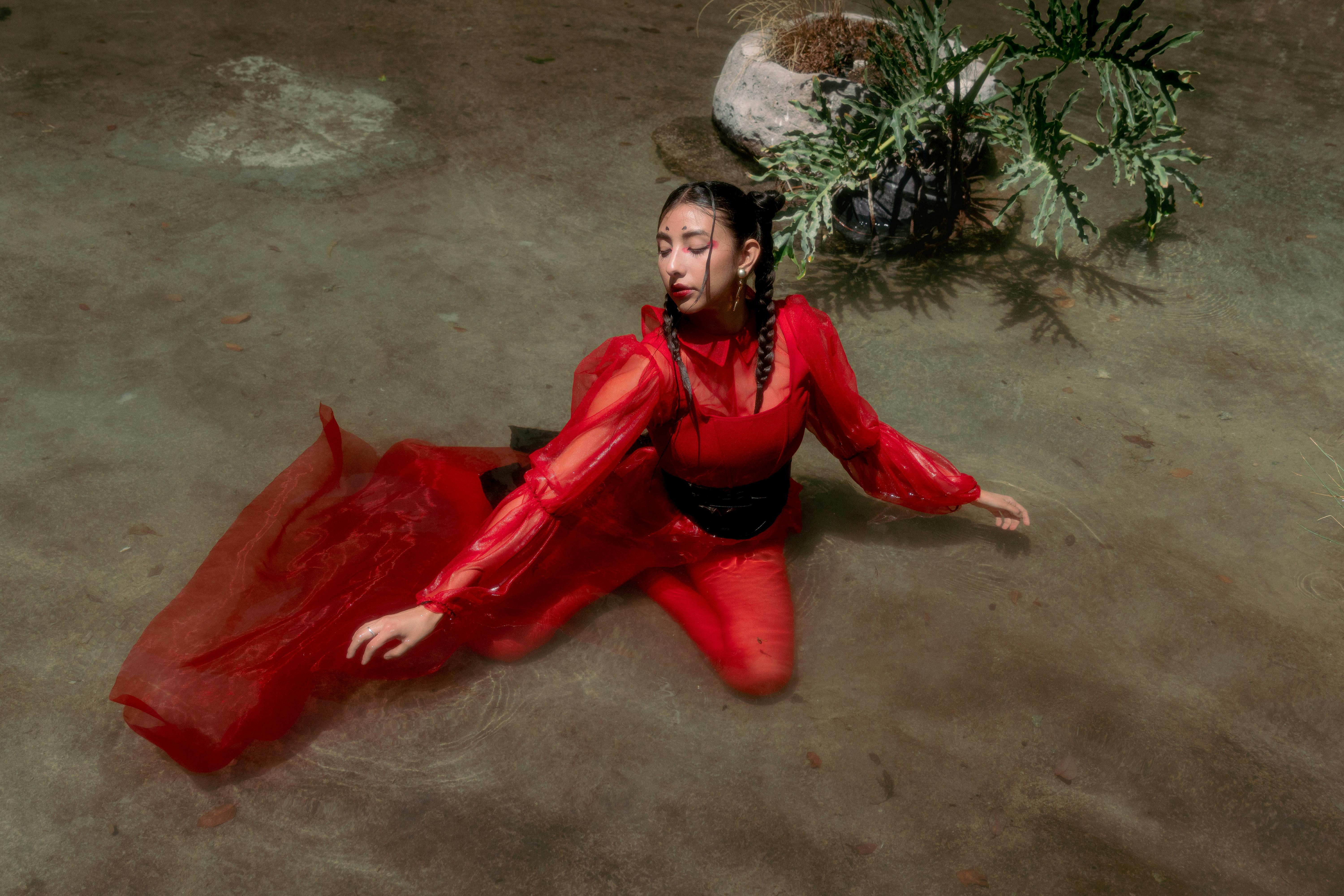 A striking image of a woman in a red dress posing gracefully in shallow water.