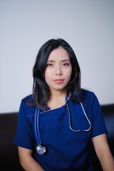 Portrait of a young female nurse in blue uniform with a stethoscope, looking confident indoors.