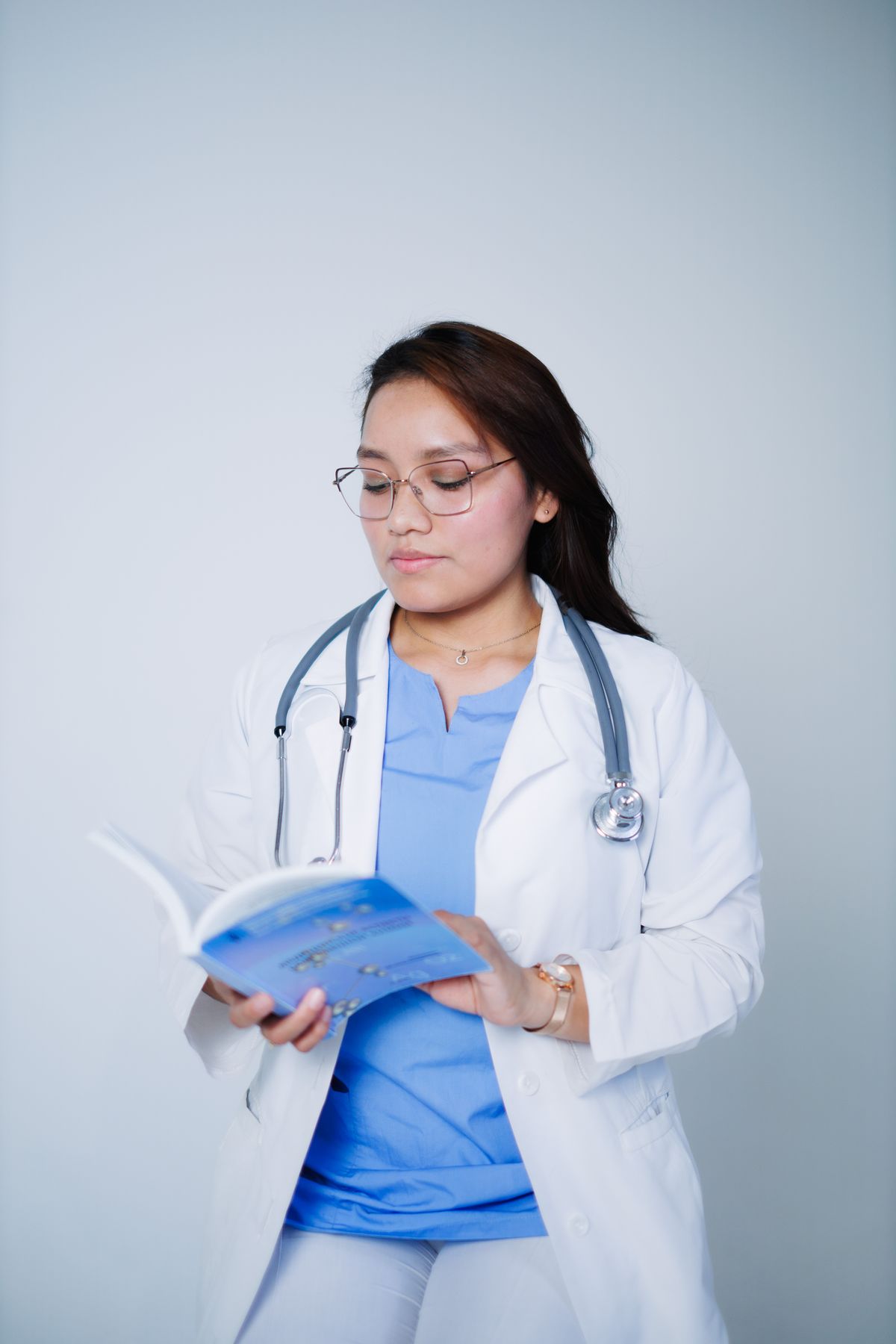 A doctor in a white coat and glasses reading a medical book