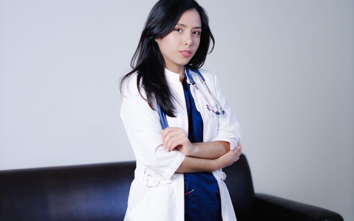 Portrait of a confident female doctor standing in a clinical setting, arms crossed.