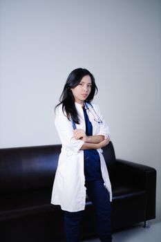 Portrait of a confident female doctor standing in a clinical setting, arms crossed.