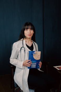 Young female doctor in lab coat with stethoscope, holding a book on electrocardiography.