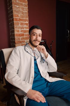 Young male doctor smiling in a modern clinic with a stethoscope, creating a welcoming atmosphere.