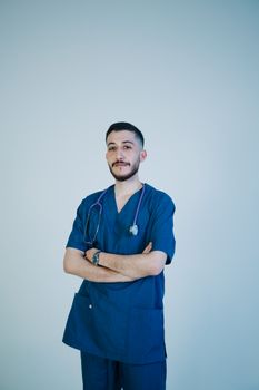 Portrait of a confident young male healthcare professional in scrubs with crossed arms and stethoscope.