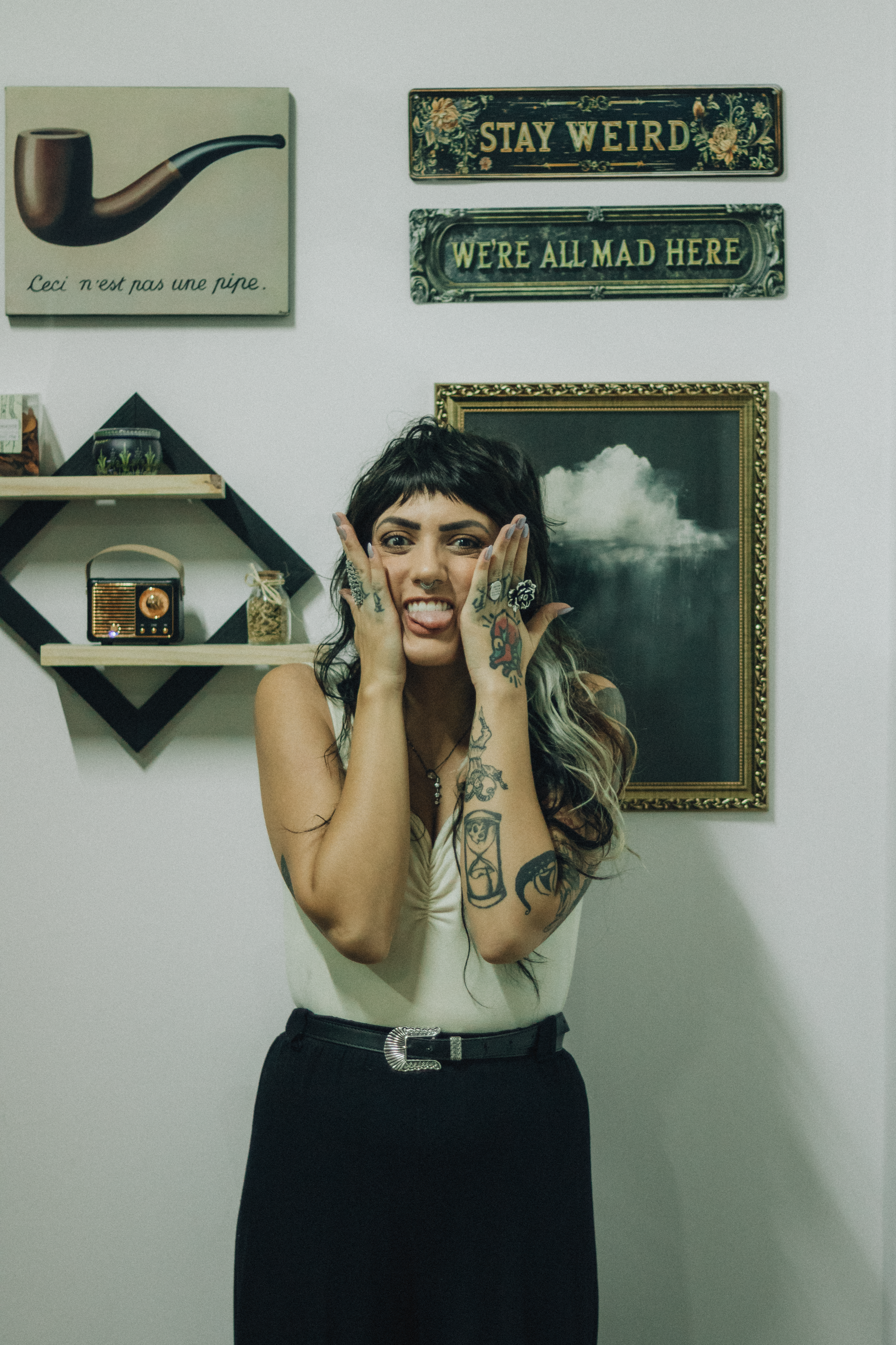 Tattooed woman making a funny face surrounded by quirky art and decor indoors.