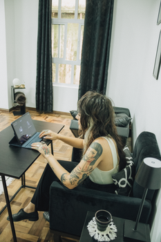 Woman with tattoos using a laptop in a cozy home setting, focusing on work.