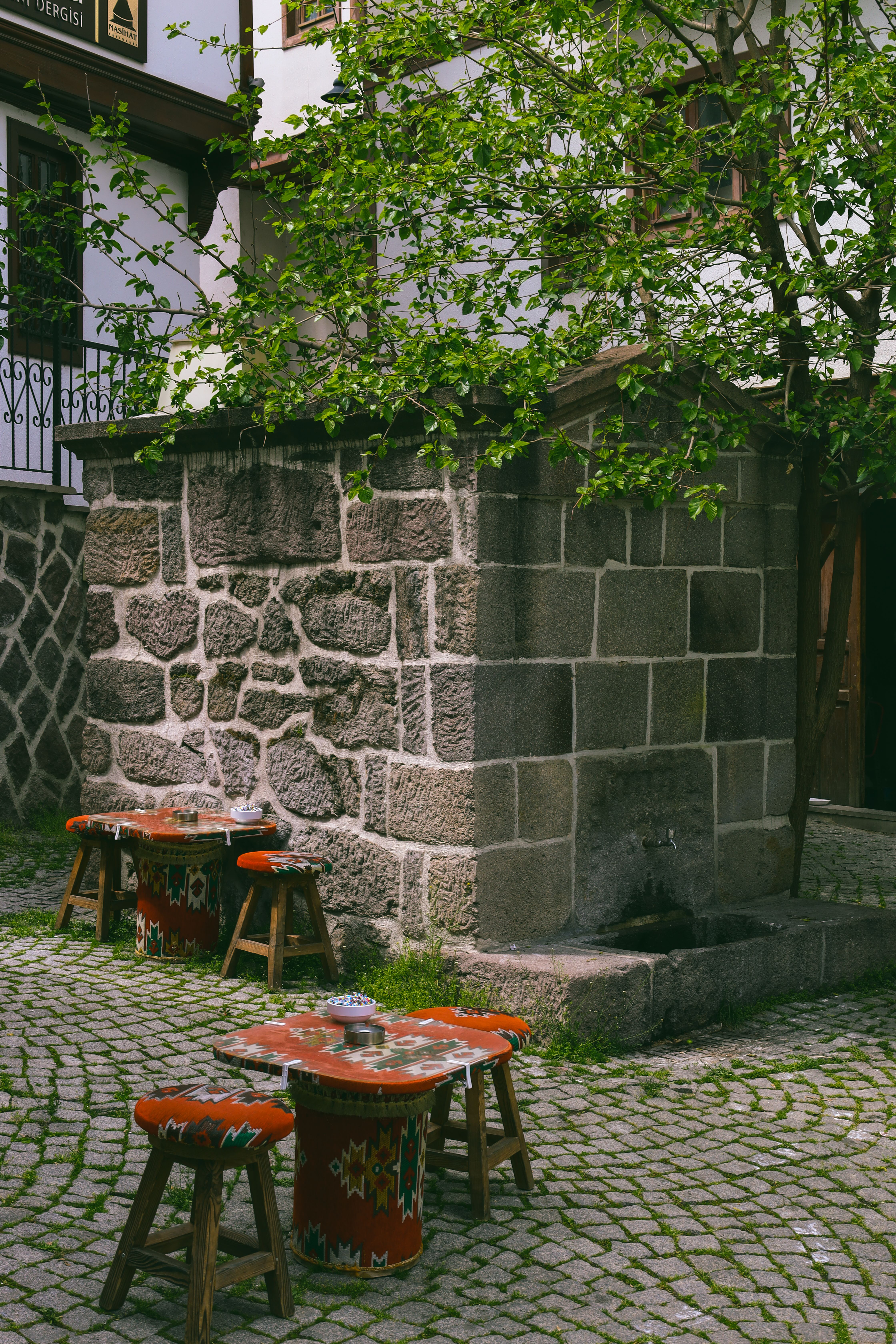 A cozy outdoor plaza with a historical stone fountain and colorful stools in Ankara, Türkiye.