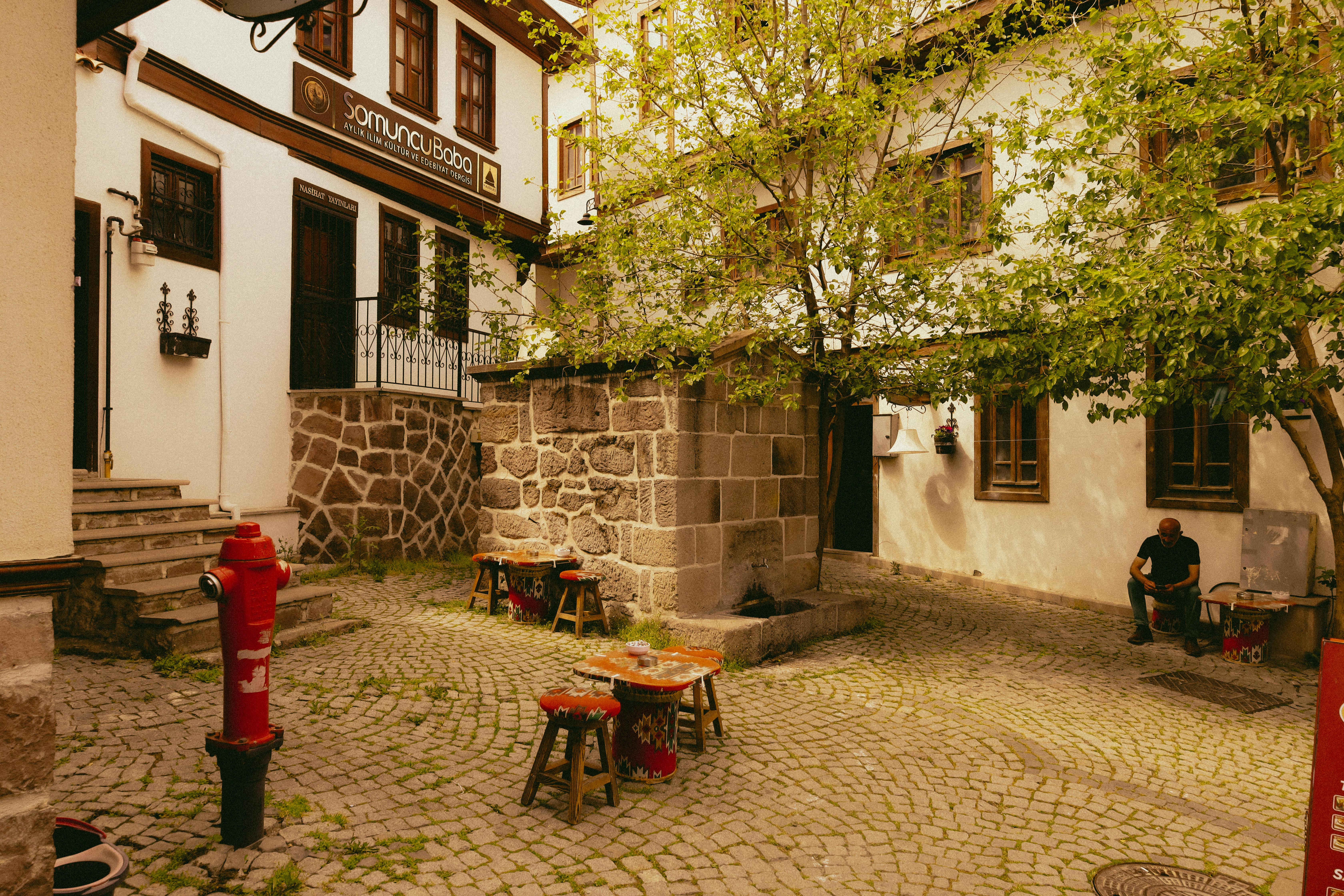 Gratuit Cafenea pitorească în aer liber, cu o fântână istorică din piatră, într-o curte pavată cu piatră cubică. Fotografie de stoc