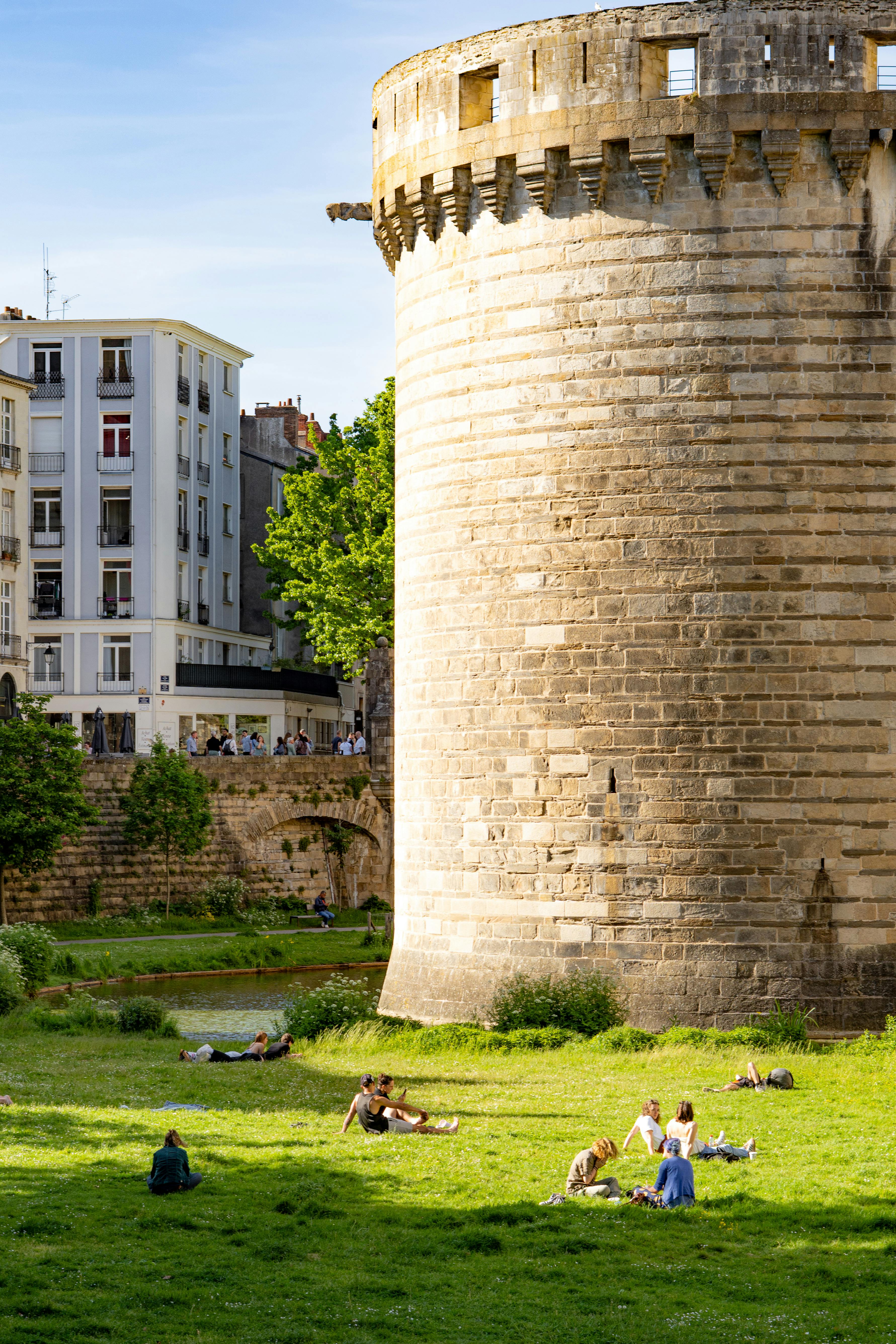 People enjoying a sunny day near historic castle in Nantes, France.